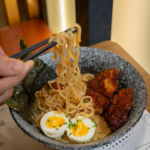 persona comiendo ramén de pollo, con fideos, huevo y alga nori. Palitos de sushi.