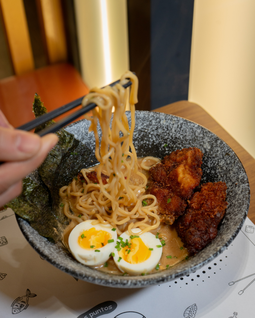 persona comiendo ramén de pollo, con fideos, huevo y alga nori. Palitos de sushi.